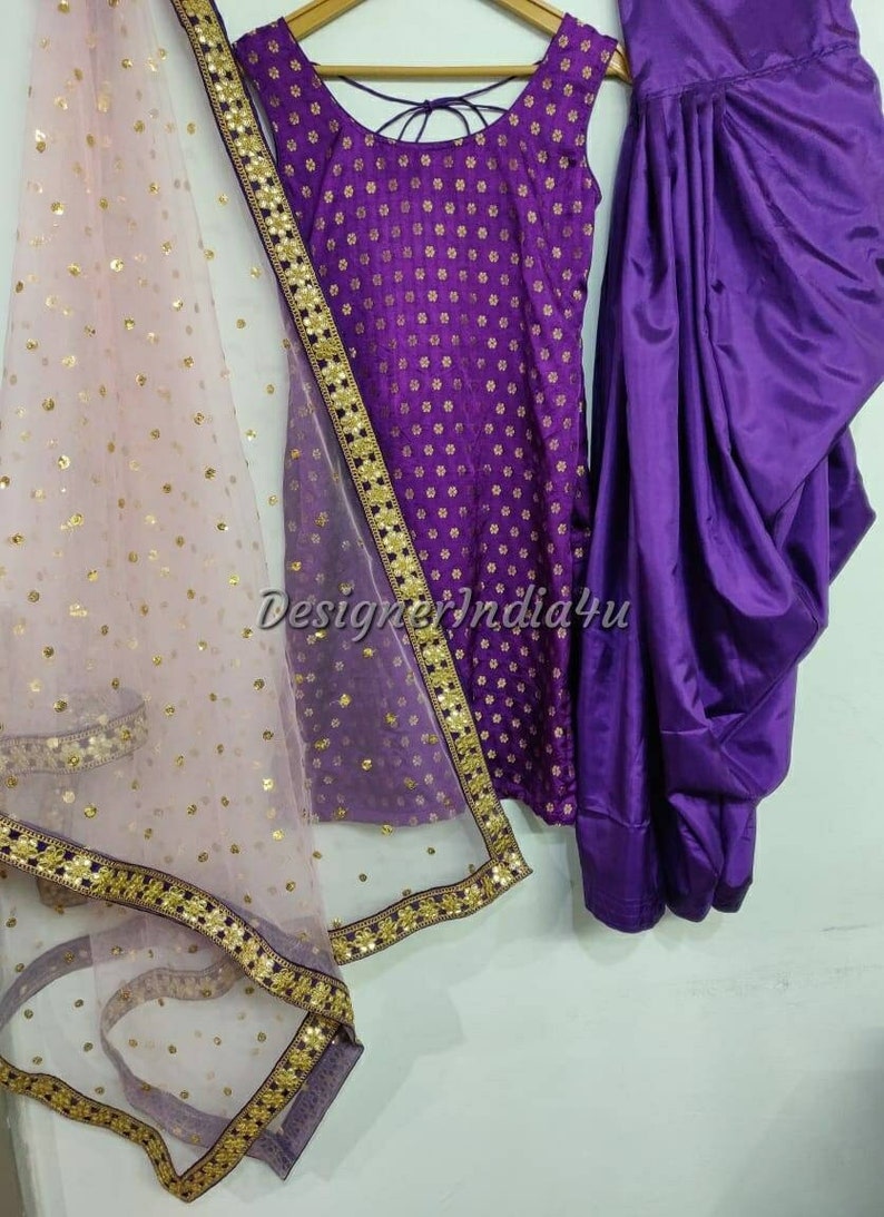 Op de afbeelding: Een paarse en gouden salwar kameez set met een doorschijnende dupatta. De kameez heeft een ronde halslijn en een mouwloos ontwerp. De salwar is een broek met een dhoti-stijl. De dupatta is een doorschijnende sjaal met een gouden rand.