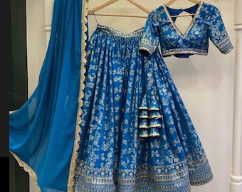 May include: A blue and silver Indian bridal outfit featuring a long skirt, a matching blouse, and a sheer dupatta. The skirt has a floral print and a silver border. The blouse has a V-neckline and a silver trim. The dupatta is sheer and has a silver border.