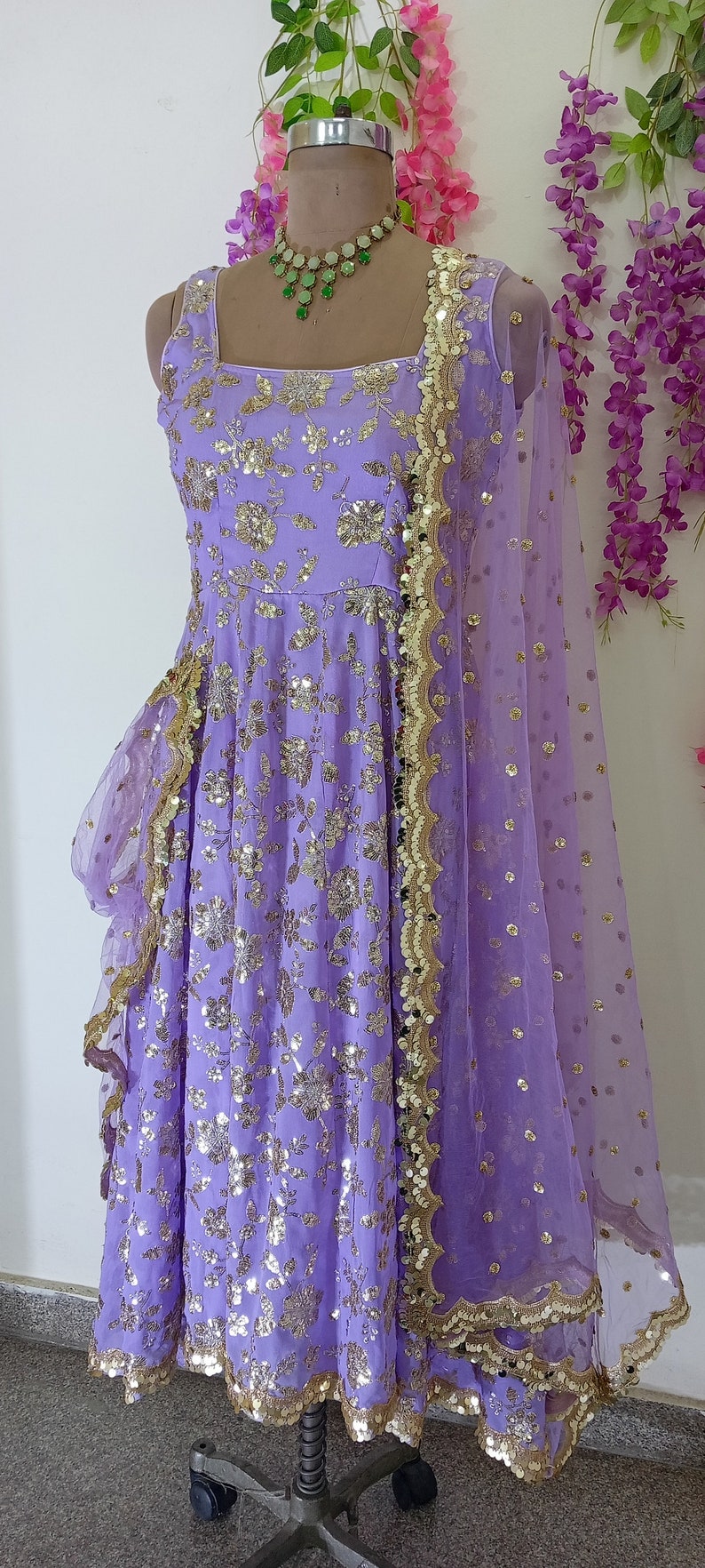 May include: A lavender-colored dress with gold sequins and a matching sheer dupatta. The dress has a ruffled hem and a square neckline. The dupatta has a scalloped border.