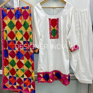 Pu&ograve; includere: Un set salwar kameez bianco con ricami colorati. Il kameez ha una scollatura rotonda e maniche lunghe. Il salwar &egrave; un paio di pantaloni larghi. Il dupatta &egrave; una lunga sciarpa con un motivo geometrico colorato.