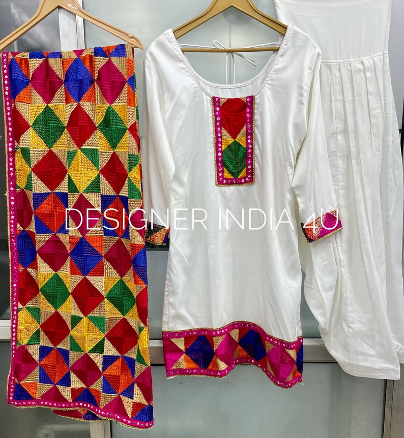 Pu&ograve; includere: Un set salwar kameez bianco con ricami colorati. Il kameez ha una scollatura rotonda e maniche lunghe. Il salwar &egrave; un paio di pantaloni larghi. Il dupatta &egrave; una lunga sciarpa con un motivo geometrico colorato.