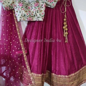 Puede incluir: Una falda de seda magenta con bordados dorados y un dupatta de red a juego. La falda tiene un cierre de cord&oacute;n y una borla dorada. La blusa es verde claro con bordados florales.