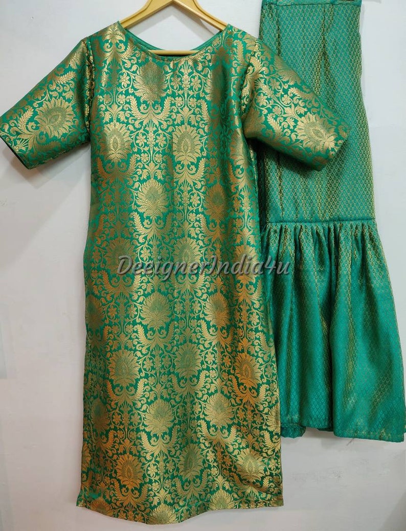 May include: A green and gold brocade ensemble featuring a tunic and matching pants. The tunic has short sleeves and a round neckline. The fabric is patterned with a floral design. The pants have a flared hem. The text "DesignerIndia4u" is visible.