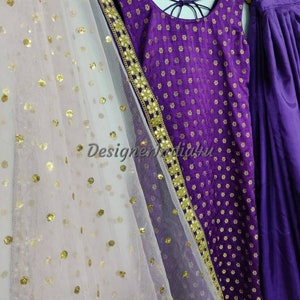Op de afbeelding: Een paarse en gouden geborduurde jurk met een witte net dupatta. De jurk heeft een ronde halslijn en is mouwloos. De dupatta heeft gouden pailletten.