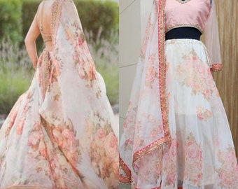 Puede incluir: Un lehenga de estampado floral blanco y rosa con un top corto rosa y un dupatta transparente. El lehenga tiene un borde dorado y rosa y el dupatta tiene un borde dorado y rosa con lentejuelas.