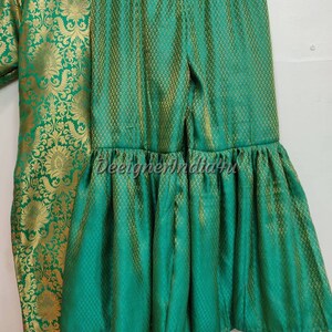 May include: A green and gold brocade outfit, including a top and flared pants. The fabric has a detailed floral pattern. The pants have a ruffled hem. The outfit is displayed on a hanger.