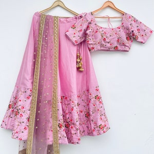 May include: A pink and floral embroidered lehenga with a matching pink embroidered blouse and a sheer pink dupatta with gold trim.