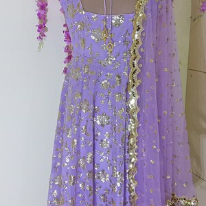 May include: A lavender-colored dress with gold sequins and a matching sheer dupatta. The dress has a scoop neckline and a tie-up back.