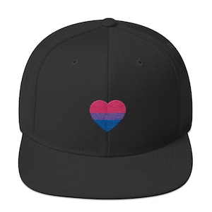 Peut inclure: Casquette de baseball noire à visière plate, ornée d'un cœur brodé aux couleurs du drapeau de la fierté bisexuelle : rose, violet et bleu. La casquette a une coupe structurée, idéale pour un usage décontracté.