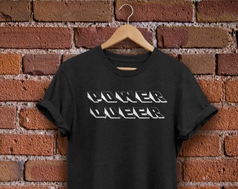 May include: Black t-shirt with white text that reads "COKER QUEER" in a 3D style.
