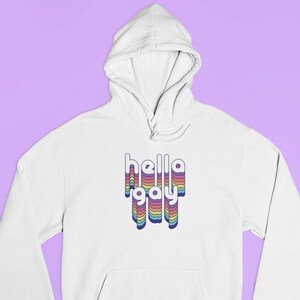 Op de afbeelding: Witte hoodie met een regenboogkleurige "hello gay" afbeelding op de voorkant.
