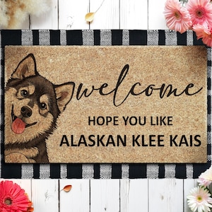 May include: A rectangular doormat with a smiling Alaskan Klee Kai dog illustration and the word "welcome" in cursive. The text "HOPE YOU LIKE ALASKAN KLEE KAIS" is also displayed. The mat has a black and white checkered border.