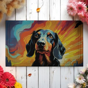 May include: Rectangular doormat featuring a stylized portrait of a dachshund dog. The dog has black fur with brown accents, set against a vibrant background of orange, yellow, and blue hues. The doormat is bordered with a darker trim.