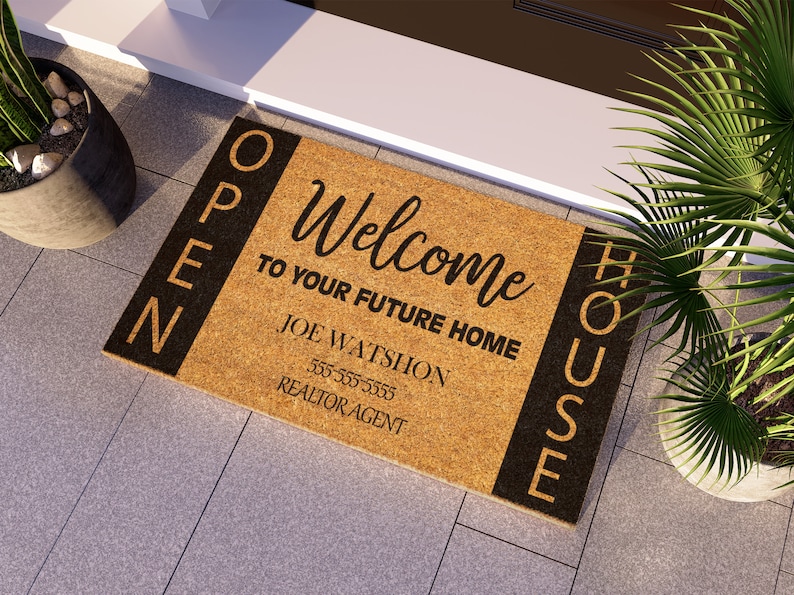 Op de afbeelding: Een bruine kokosmat met de tekst "OPEN HOUSE" aan de zijkanten en "Welcome to your future home" in het midden. De tekst "Joe Wattshon Realtor Agent 555-555-5555" staat eronder gedrukt.