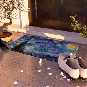 May include: A blue and yellow doormat with a swirling pattern reminiscent of Van Gogh's Starry Night. The doormat is placed on a brown tiled floor with white flower petals scattered around it. Two pairs of shoes are placed on the floor, one pair is black heels and the other pair is white leather shoes.
