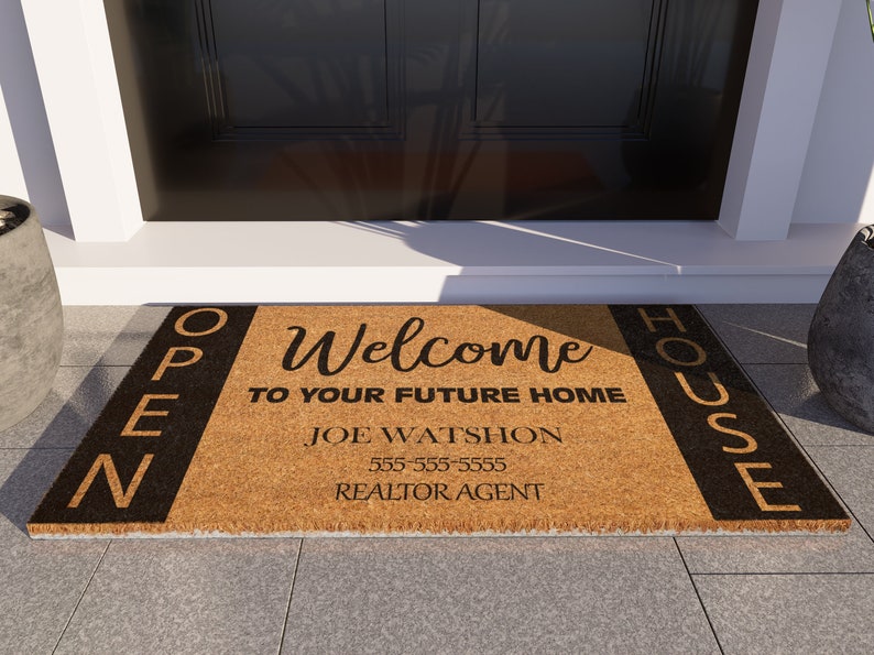 Op de afbeelding: Een bruine kokosmat met zwarte letters die "OPEN HOUSE" aan de linker- en rechterkant aangeven. Het midden van de mat geeft "Welcome to your future home" aan met de naam "Joe Watson" en een telefoonnummer eronder. De tekst "Realtor Agent" staat onderaan.