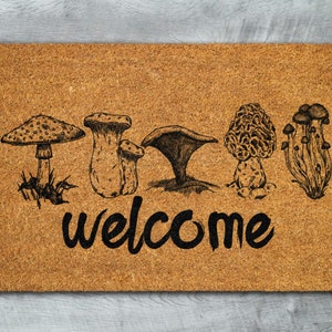 May include: A brown coir doormat with a welcome message and a row of five black and white mushroom illustrations.