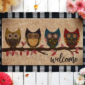 May include: Rectangular doormat featuring four colorful owls perched on a branch, with the word "welcome" in black script. The owls are brown, orange, blue, and red, with intricate patterns. The mat has a natural, textured background.