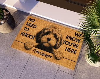 May include: A brown coir doormat with the text "No need to knock - We know you're here - The Cavapoo" and a black and white illustration of a Cavapoo dog peeking over the top.