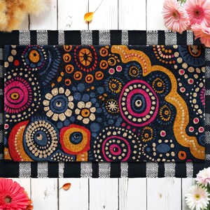 May include: A rectangular doormat with a black background and a colorful, circular design. The design includes pink, orange, blue, and gold patterns. The mat is bordered by a black and white checkered pattern.