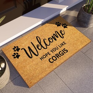 May include: A brown coir doormat with the text "Welcome Hope you like Corgis" and two paw prints on the left and three paw prints on the right.