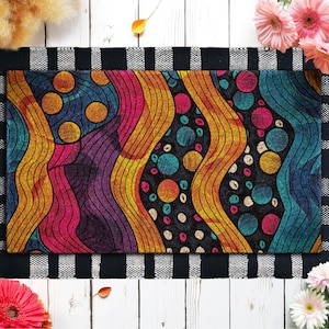 May include: Rectangular doormat with a vibrant abstract design. The pattern features wavy lines and circles in shades of orange, yellow, pink, purple, and teal against a black background. The mat is bordered by a black and white checkered pattern.