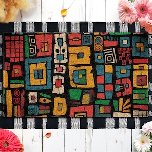 May include: A rectangular doormat with a black background and a colorful geometric pattern. The pattern includes squares and rectangles in shades of red, yellow, blue, and green. The mat is framed with a black and white striped border.