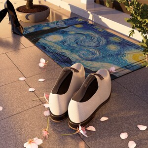 May include: A pair of white leather shoes with black laces sit on a tiled floor with pink flower petals scattered around them. A blue and yellow doormat with a swirling pattern is in the background.