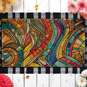 May include: A rectangular doormat with a colorful stained-glass design. The mat features a black and white checkered border. The design includes swirls and geometric shapes in shades of red, orange, yellow, green, and blue.