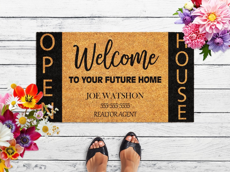 Op de afbeelding: Een bruine kokosmat met zwarte letters die aan de zijkanten "Open House" en in het midden "Welcome to your future home Joe Watshon 555-555-5555 Realtor Agent" staat.
