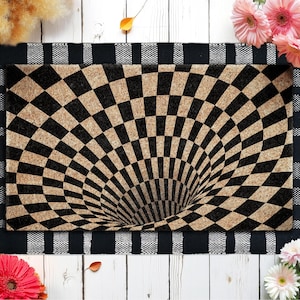 May include: A rectangular doormat with a black and tan checkered pattern that creates a 3D optical illusion of a hole. The mat is bordered by a black and white striped design.