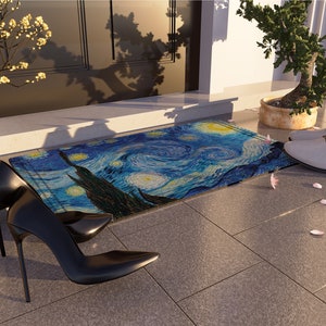 May include: A blue and yellow doormat with a painting of a starry night. The doormat is on a gray tiled floor with pink flower petals scattered around it. Two black high-heeled shoes are on the floor next to the doormat.