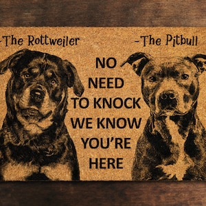May include: A brown doormat with a black and white image of a Rottweiler and a Pitbull. The text on the doormat reads "The Rottweiler - No Need To Knock We Know You're Here - The Pitbull".