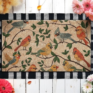 May include: Rectangular doormat featuring a detailed illustration of colorful birds perched on tree branches with green leaves. The birds are in shades of red, yellow, blue, and orange against a tan background. The mat has a black and white checkered border.