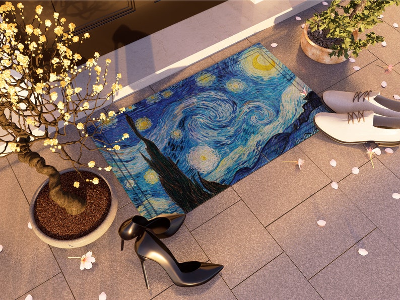 May include: A blue and yellow doormat with a swirling, starry night design. The doormat is on a gray tiled floor with white flower petals scattered around it.