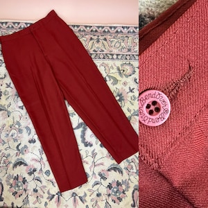 May include: A pair of red high-waisted pants with a button fly and a red button with the text "Bend Over" on it.