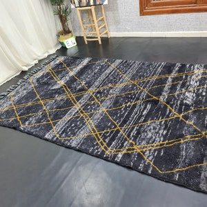 May include: A black and gray rug with a geometric pattern of yellow lines. The rug has fringe on all sides.