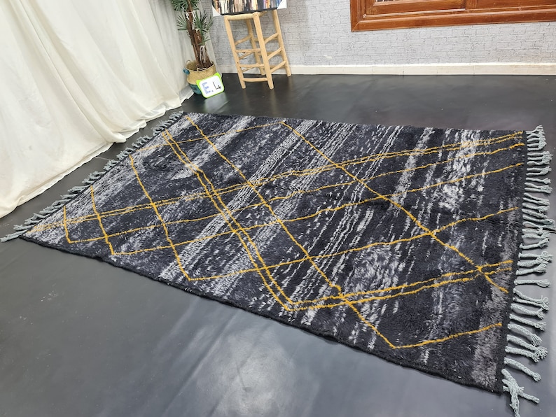 May include: A black and gray rug with a geometric pattern of yellow lines. The rug has fringe on all sides.