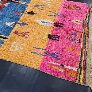 May include: A colorful Moroccan rug with a geometric pattern in shades of blue, pink, orange, and white. The rug has a fringe border and is made of wool.
