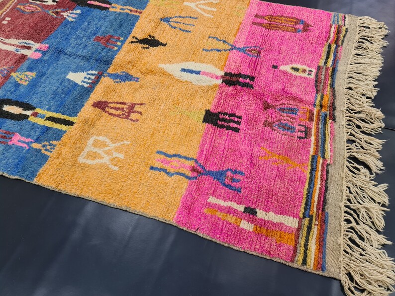 May include: A colorful Moroccan rug with a geometric pattern in shades of blue, pink, orange, and white. The rug has a fringe border and is made of wool.