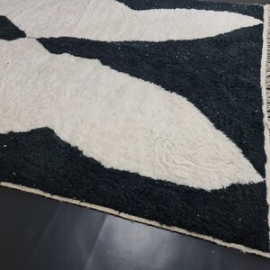 May include: Black and white rug with a geometric pattern. The rug has a fringe border.