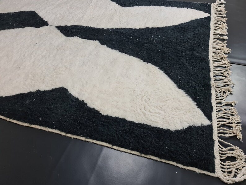 May include: Black and white rug with a geometric pattern. The rug has a fringe border.