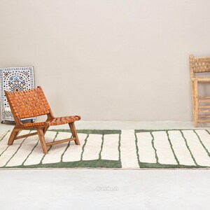 May include: A woven leather chair with a wooden frame sits on a rectangular rug with a white and green striped pattern. A decorative mosaic panel and a wooden stool are also in the image. The rug has a fringe.