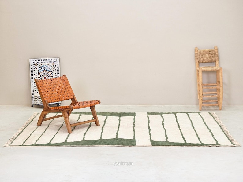 May include: A woven leather chair with a wooden frame sits on a rectangular rug with a white and green striped pattern. A decorative mosaic panel and a wooden stool are also in the image. The rug has a fringe.