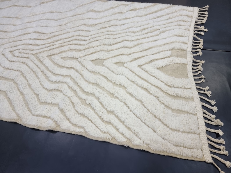 May include: A white, fluffy rug with a wavy, abstract pattern. The rug has a fringe border.