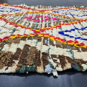 May include: A white, brown, blue, red, and yellow woven rug with a fringe border. The rug has a geometric pattern with circles and stripes.