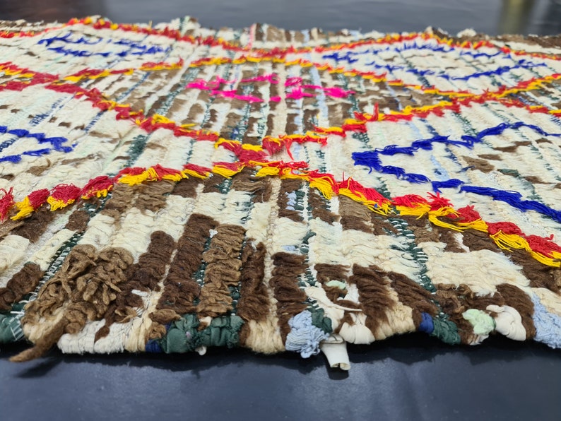 May include: A white, brown, blue, red, and yellow woven rug with a fringe border. The rug has a geometric pattern with circles and stripes.