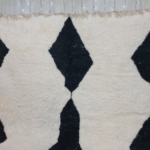 May include: A white and black Moroccan rug with a diamond pattern. The rug has a fluffy texture and is made of wool.