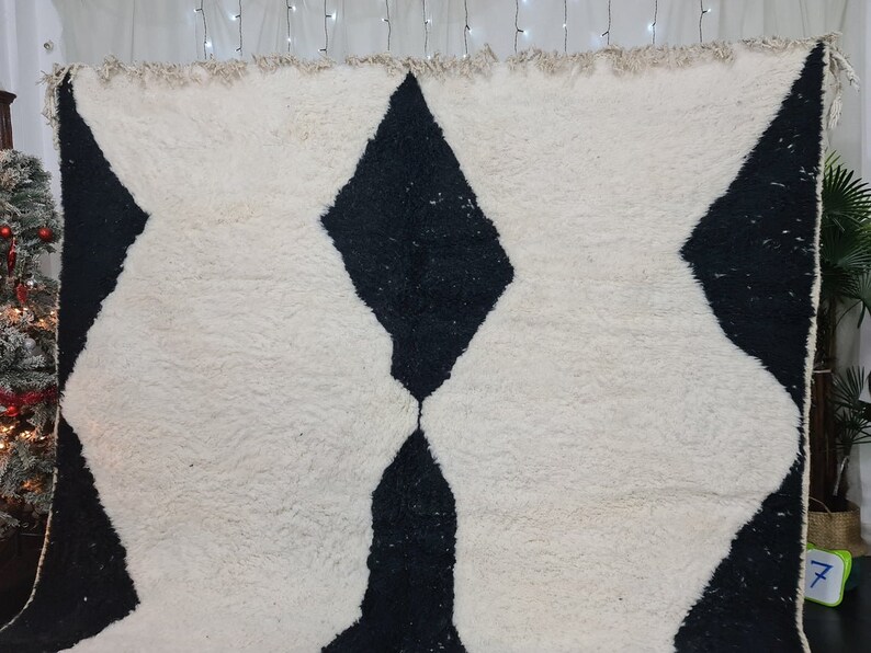 May include: A white and black Moroccan rug with a diamond pattern. The rug has a fluffy texture and is made of wool.