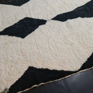 May include: A white and black geometric patterned rug with a fringe border. The rug has a fluffy texture.